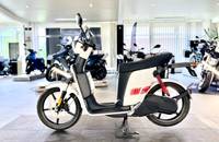 Seitenansicht eines weißen Elektro-Scooters, der in einem hellen Showroom auf einem Boden präsentiert wird.