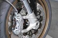 Nahaufnahme der Bremsanlage eines Motorrads mit silbernem Bremssattel und perforierter Bremsscheibe.